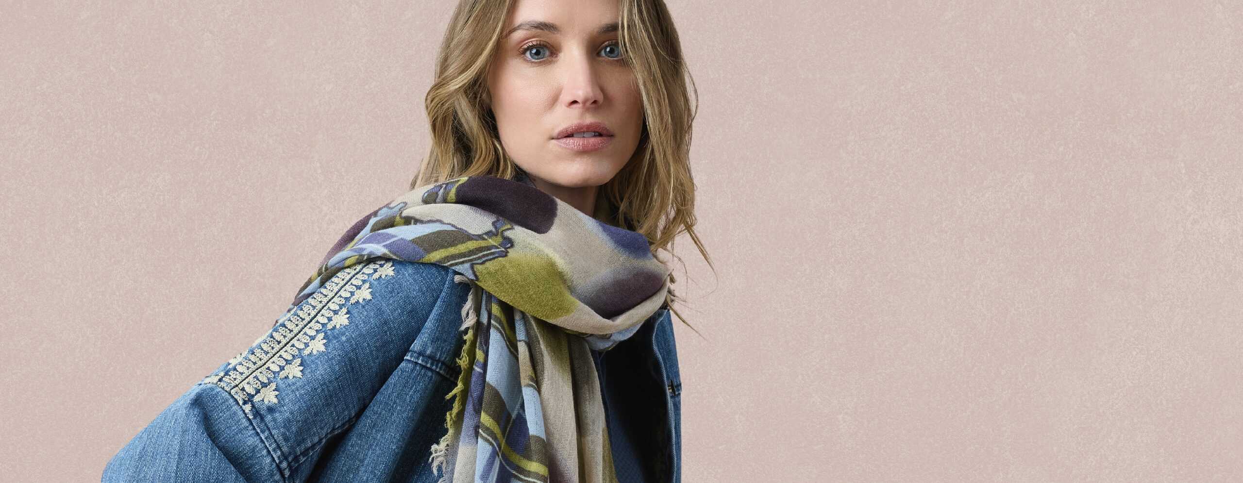 Woman wearing a Storiatipic scarf with blue, khaki and plum patterns over an embroidered denim jacket